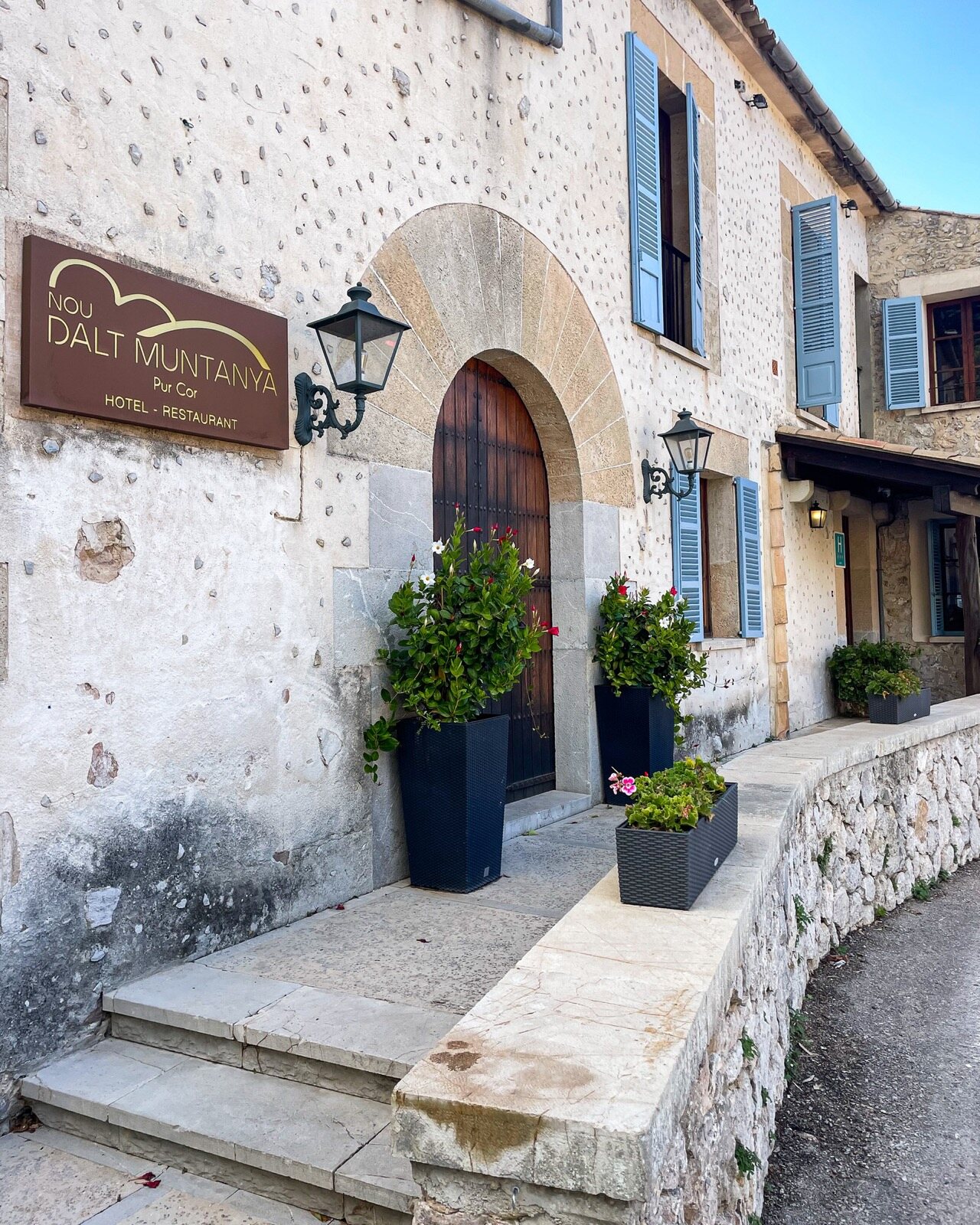 The hotel entrance: a stone doorway with a Dalt Muntanya sign, potted plants and steps up from the lane