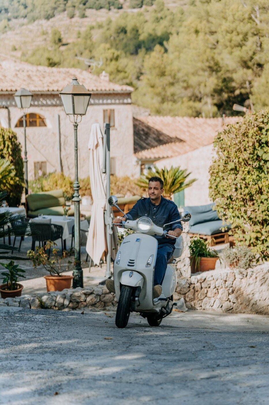 A narrow stone lane in the village of Orient with a parked Vespa, an archway and the mountains rising at the end of the street