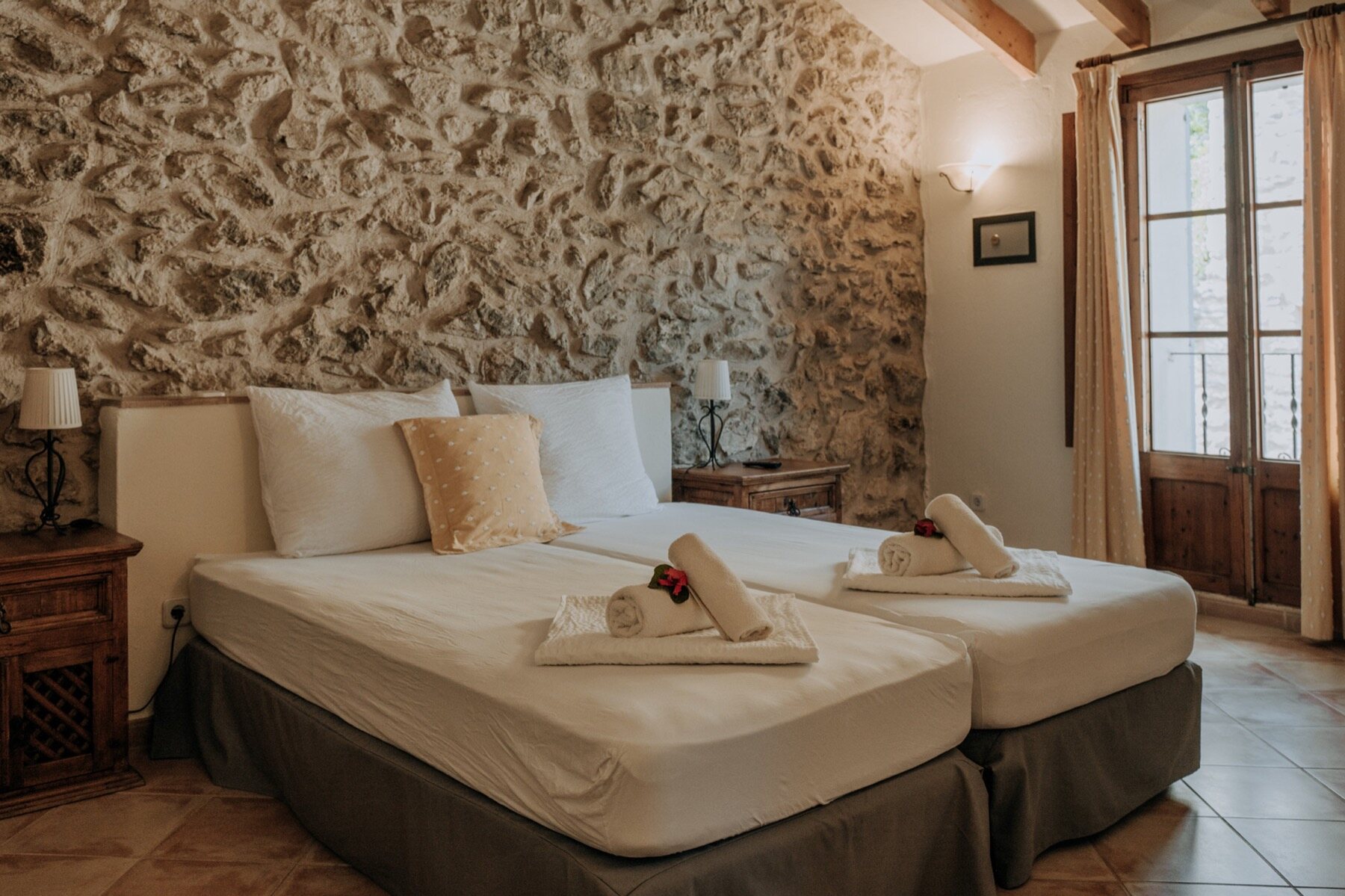 A calm room with a bare stone accent wall, a double bed in white linen and doors opening to the terrace and the mountainside