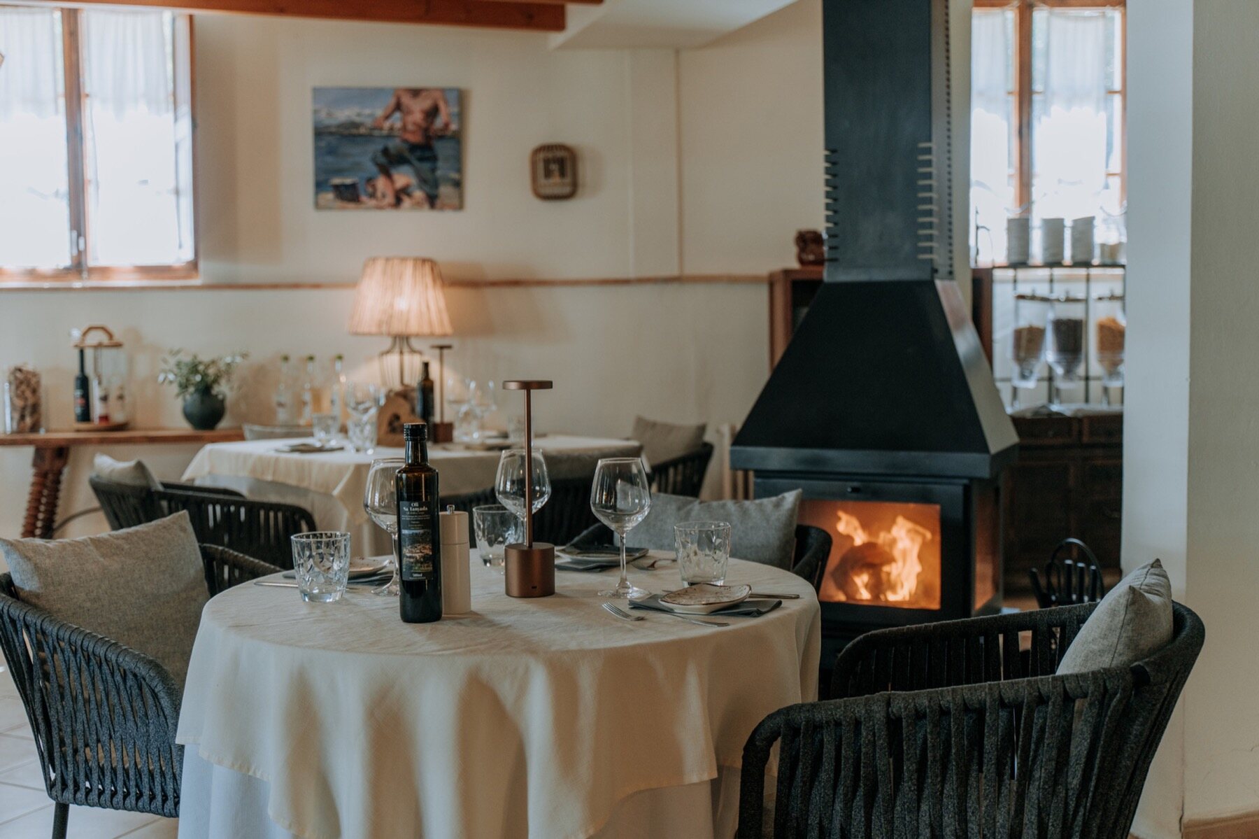 The dining room with a lit stone fireplace, tables set with white cloths and wine, warm lamplight on rendered walls