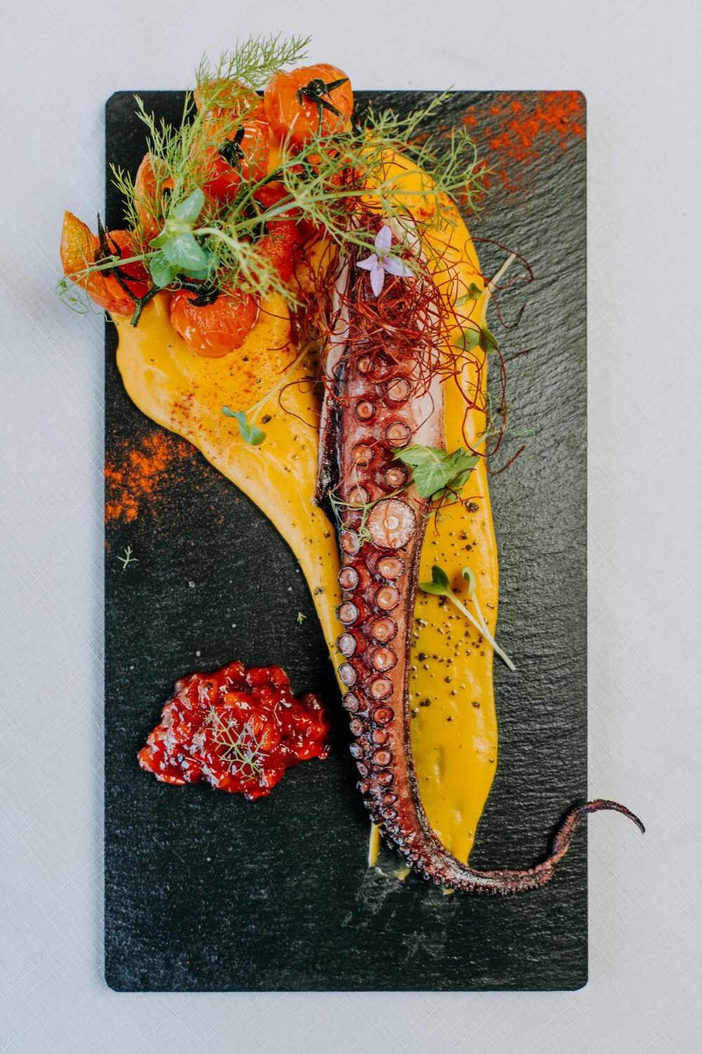 A plated octopus dish with saffron and tomato on dark slate, restaurant plating at Es Freu